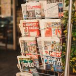 Stack of diverse newspapers in a metal stand, showcasing media variety.
